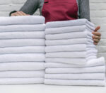 A lot of white towels on the white table and worker in laundry or hotel on white background