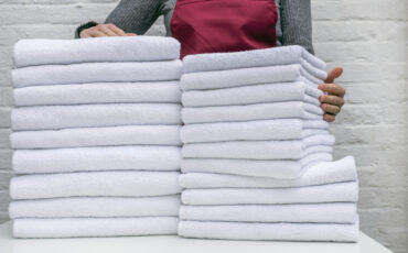 A lot of white towels on the white table and worker in laundry or hotel on white background