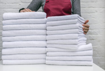 A lot of white towels on the white table and worker in laundry or hotel on white background