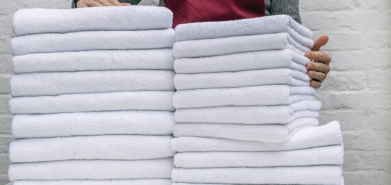 A lot of white towels on the white table and worker in laundry or hotel on white background