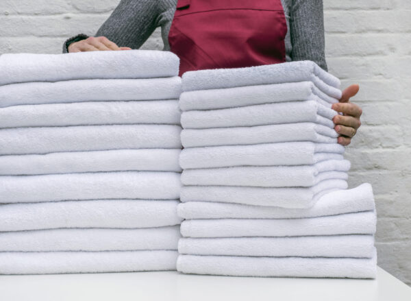 A lot of white towels on the white table and worker in laundry or hotel on white background