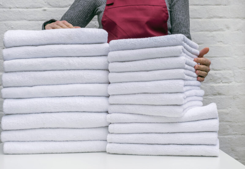 A lot of white towels on the white table and worker in laundry or hotel on white background